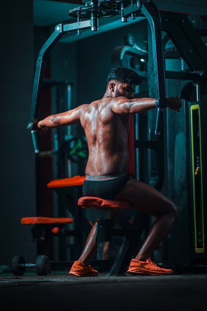 A shirtless man demonstrating strength while using gym equipment indoors for fitness.